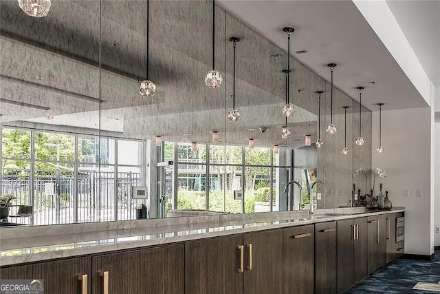 bar with dark brown cabinetry, hanging light fixtures, light stone counters, and vaulted ceiling