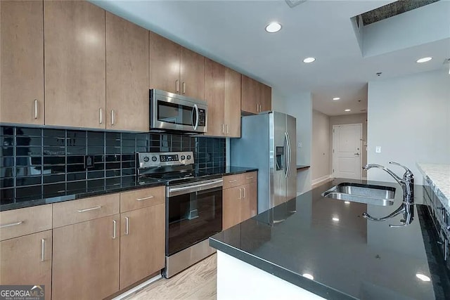 kitchen with sink, appliances with stainless steel finishes, dark stone counters, light hardwood / wood-style floors, and decorative backsplash