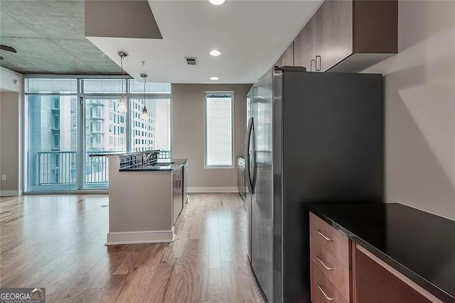 kitchen featuring sink, hanging light fixtures, light wood-type flooring, stainless steel refrigerator, and dark stone counters