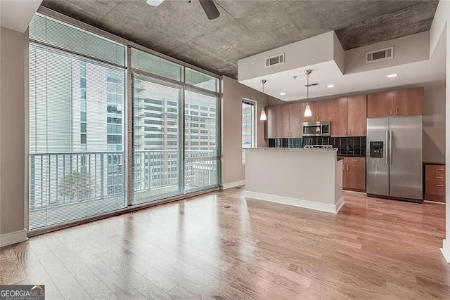 kitchen featuring pendant lighting, a wall of windows, stainless steel appliances, light hardwood / wood-style floors, and decorative backsplash