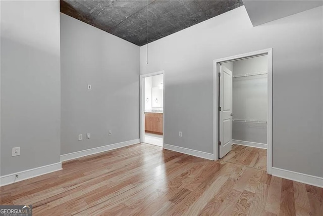 unfurnished bedroom featuring a walk in closet, ensuite bath, a closet, and light hardwood / wood-style flooring