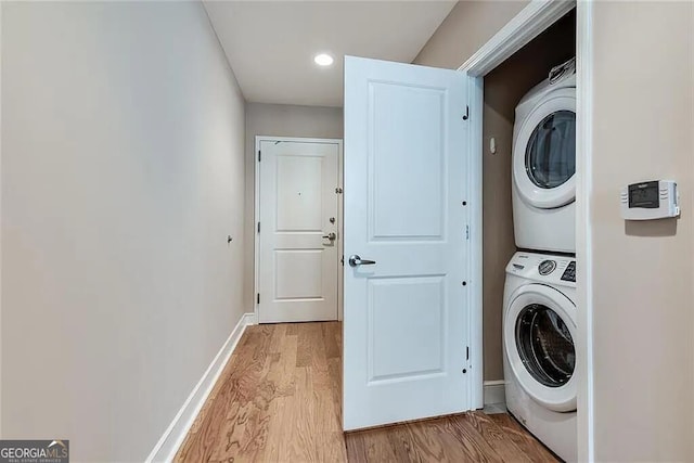 laundry room with stacked washer / drying machine and light hardwood / wood-style flooring