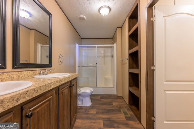 bathroom with a textured ceiling, hardwood / wood-style flooring, toilet, a shower with shower door, and vanity