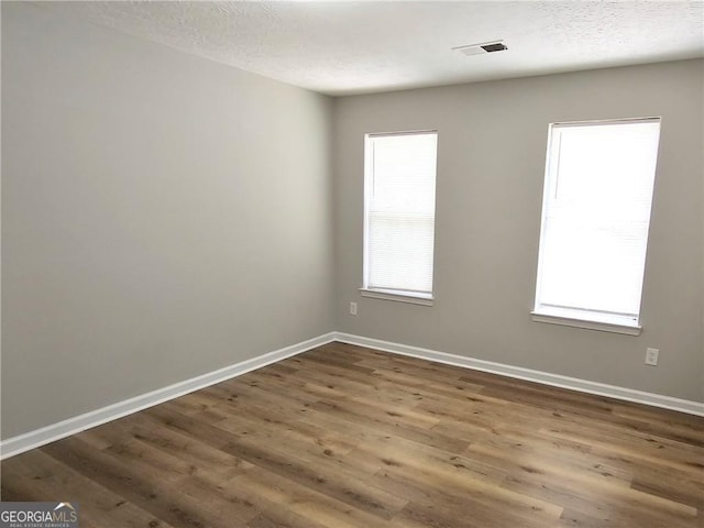 spare room featuring visible vents, a textured ceiling, baseboards, and wood finished floors