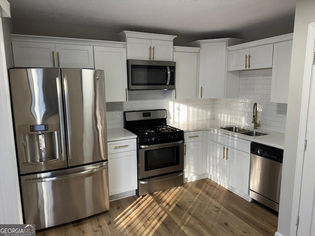 kitchen featuring white cabinets, dark wood-type flooring, stainless steel appliances, light countertops, and a sink