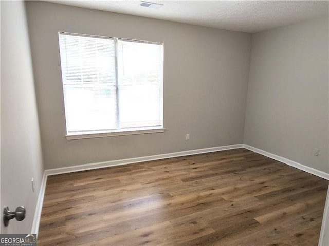 unfurnished room with visible vents, a textured ceiling, baseboards, and wood finished floors