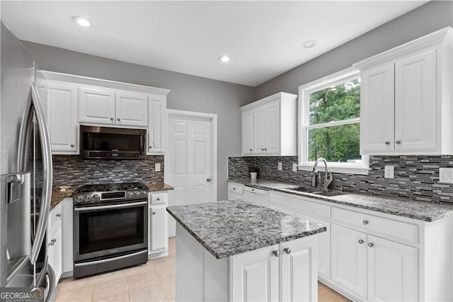 kitchen with decorative backsplash, appliances with stainless steel finishes, a kitchen island, sink, and white cabinetry