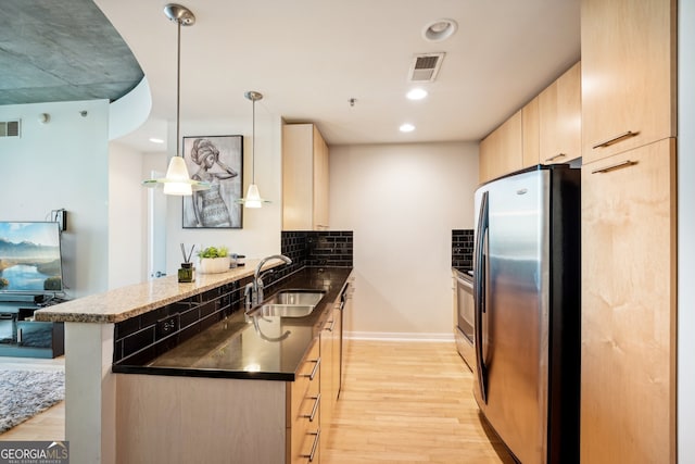 kitchen with hanging light fixtures, sink, stainless steel fridge, light wood-type flooring, and tasteful backsplash