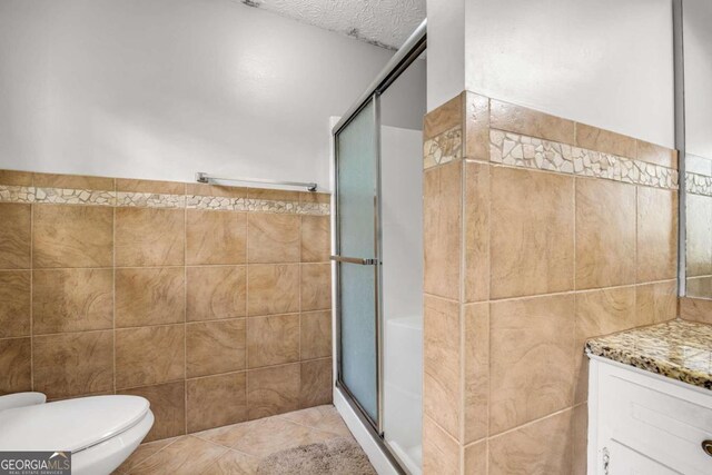 bathroom with tile walls, toilet, vanity, an enclosed shower, and tile patterned floors