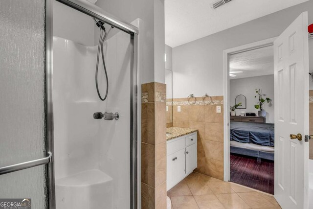 bathroom with vanity, walk in shower, tile walls, and tile patterned flooring