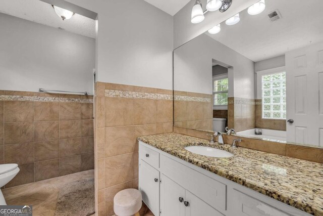 full bathroom with tile patterned floors, toilet, independent shower and bath, tile walls, and vanity