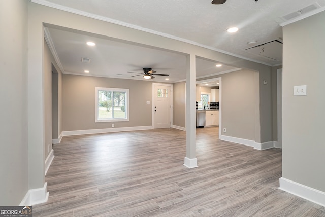 unfurnished living room featuring ceiling fan, a textured ceiling, ornamental molding, and light hardwood / wood-style flooring