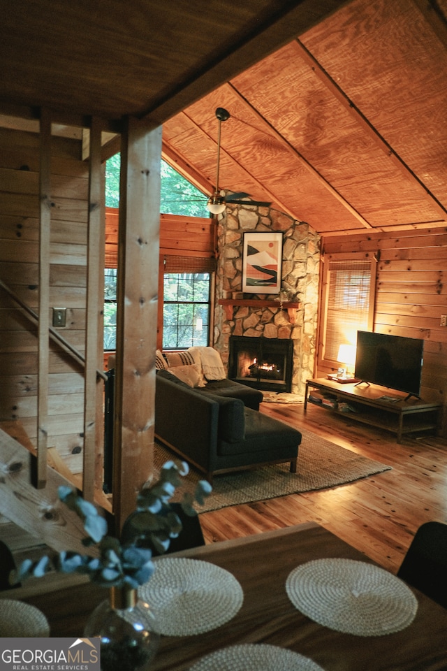 living room with wood ceiling, wood-type flooring, vaulted ceiling with beams, wood walls, and a stone fireplace