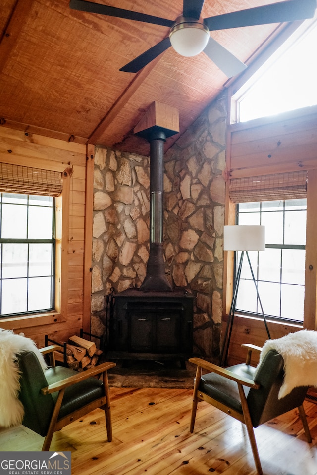 living room with hardwood / wood-style floors, vaulted ceiling, a wood stove, and wooden walls