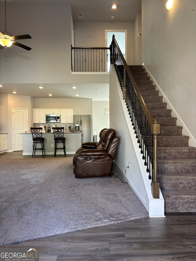 staircase with a high ceiling, hardwood / wood-style floors, and ceiling fan