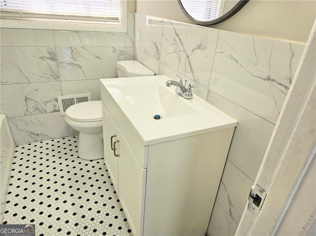 bathroom with toilet, visible vents, tile walls, and vanity