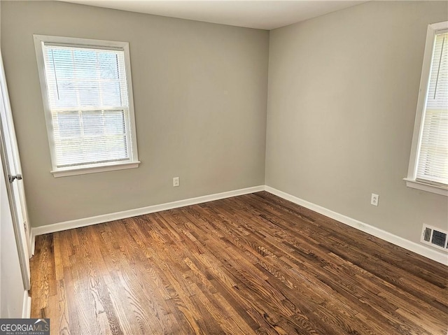 spare room featuring dark wood-style floors, visible vents, and baseboards