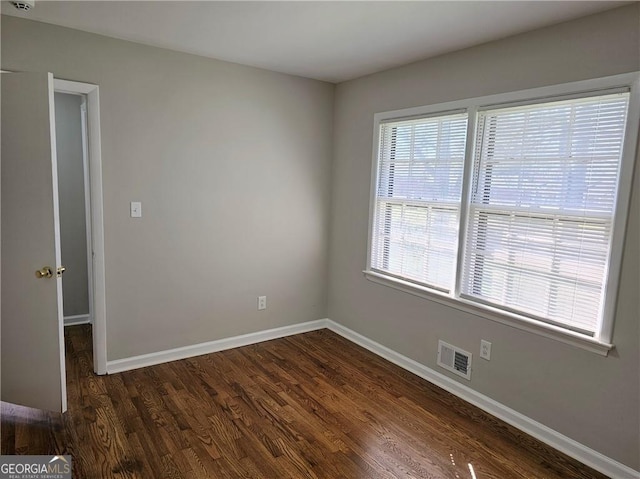 empty room with dark wood-style floors, visible vents, and baseboards