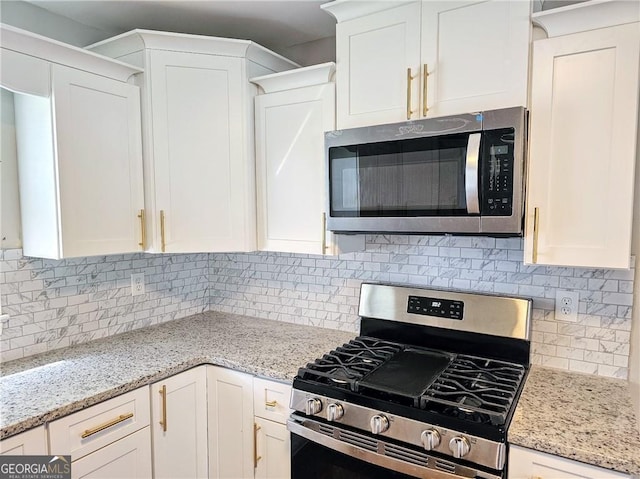 kitchen with stainless steel appliances, tasteful backsplash, light stone countertops, and white cabinets