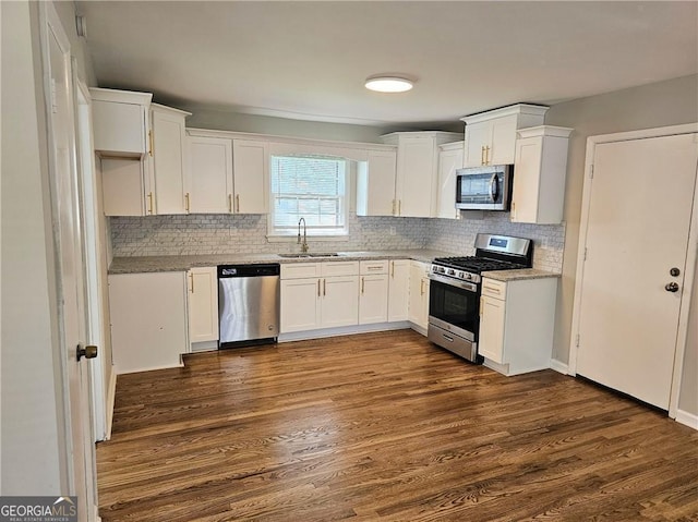 kitchen featuring white cabinets, decorative backsplash, dark wood-type flooring, stainless steel appliances, and a sink