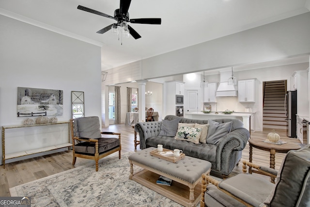 living room with decorative columns, crown molding, light wood-type flooring, and ceiling fan