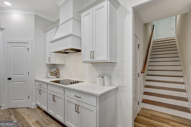 kitchen with black electric stovetop, white cabinets, premium range hood, and light hardwood / wood-style floors