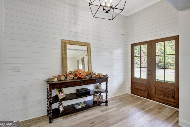 entrance foyer with french doors, wooden walls, a notable chandelier, light wood-type flooring, and a towering ceiling