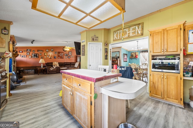 kitchen with ceiling fan with notable chandelier, decorative light fixtures, lofted ceiling, stainless steel microwave, and light wood-type flooring