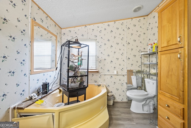 bathroom featuring wood-type flooring, toilet, a textured ceiling, ornamental molding, and a bath