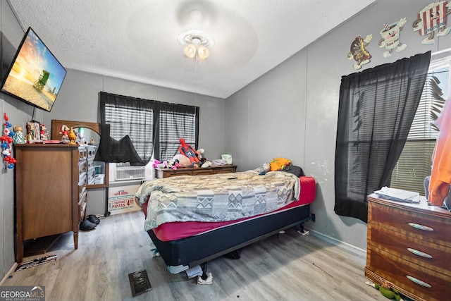 bedroom featuring light hardwood / wood-style floors, a textured ceiling, and cooling unit