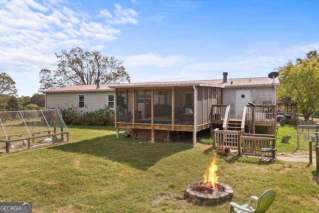 back of house with a sunroom, an outdoor fire pit, a yard, and a deck