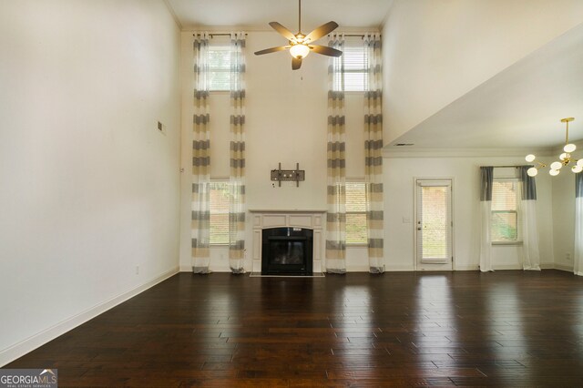 unfurnished living room featuring dark wood-type flooring, crown molding, and ceiling fan with notable chandelier