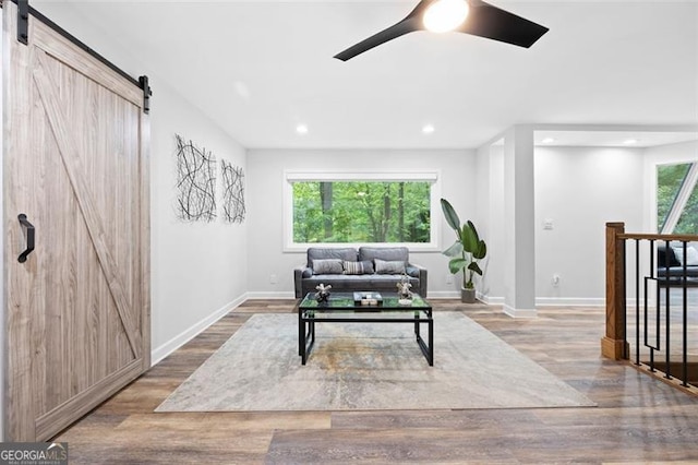 living room with ceiling fan, wood-type flooring, plenty of natural light, and a barn door