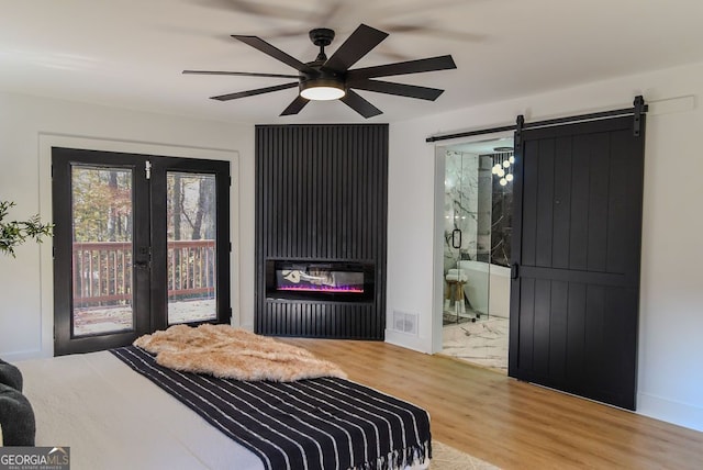 bedroom featuring access to outside, ensuite bath, ceiling fan, a barn door, and wood-type flooring