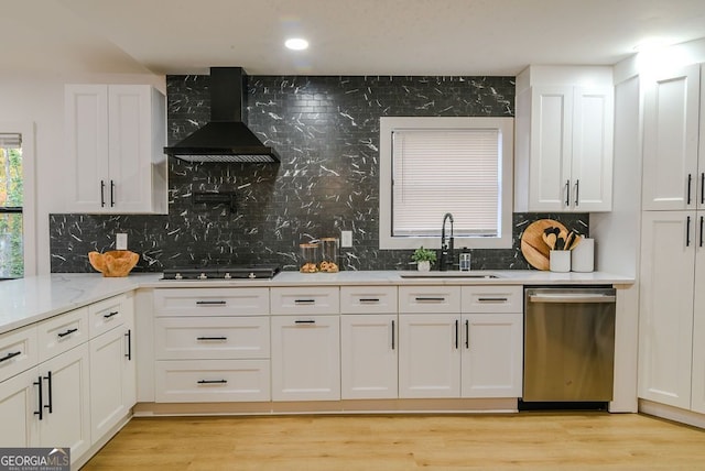 kitchen with dishwasher, wall chimney exhaust hood, sink, light hardwood / wood-style floors, and white cabinets