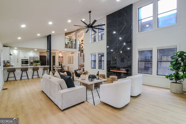 living room featuring a fireplace, light wood-type flooring, high vaulted ceiling, and ceiling fan