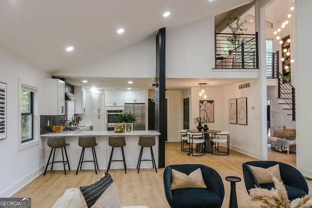 kitchen with kitchen peninsula, high vaulted ceiling, light hardwood / wood-style floors, white cabinetry, and stainless steel refrigerator