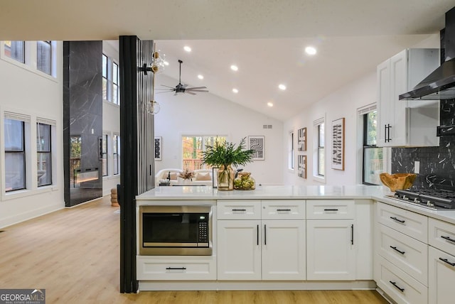 kitchen with white cabinets, stainless steel appliances, a healthy amount of sunlight, and wall chimney range hood