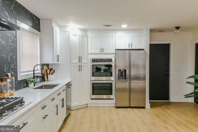 kitchen with white cabinets, sink, light hardwood / wood-style flooring, light stone counters, and stainless steel appliances