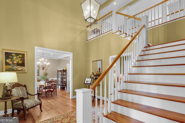 staircase featuring wood-type flooring, a notable chandelier, and a high ceiling