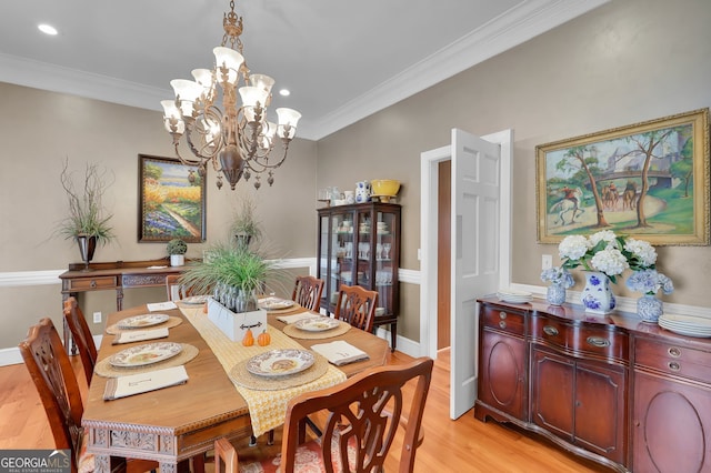 dining space with light wood-type flooring, ornamental molding, and a chandelier