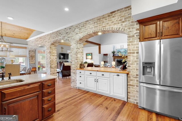 kitchen with sink, hanging light fixtures, light hardwood / wood-style flooring, stainless steel fridge with ice dispenser, and brick wall