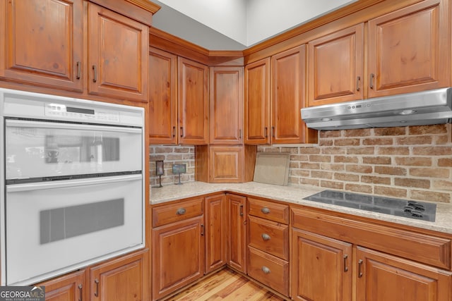 kitchen featuring backsplash, exhaust hood, electric cooktop, double oven, and light hardwood / wood-style floors