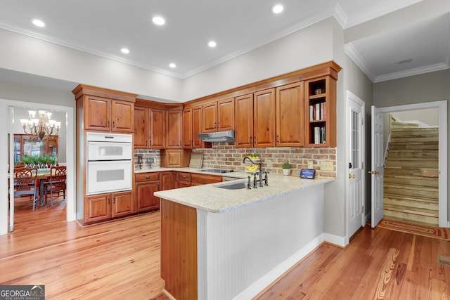 kitchen with double oven, kitchen peninsula, decorative backsplash, and light wood-type flooring