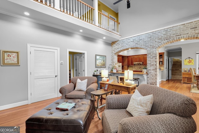 living room featuring crown molding, light hardwood / wood-style flooring, ceiling fan, a towering ceiling, and brick wall