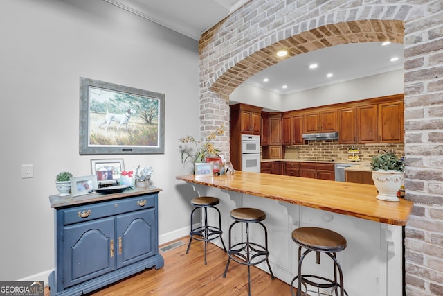 kitchen with butcher block counters, light hardwood / wood-style flooring, double oven, a breakfast bar, and ornamental molding