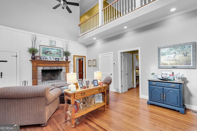 living room with ceiling fan, light wood-type flooring, a towering ceiling, a fireplace, and ornamental molding