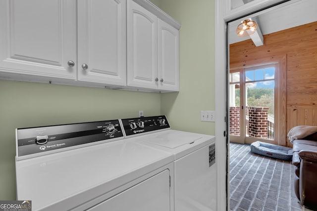 clothes washing area with wooden walls, washer and clothes dryer, and cabinets