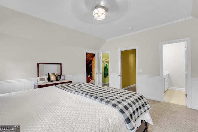 bedroom with a spacious closet, ensuite bathroom, light colored carpet, lofted ceiling, and a closet