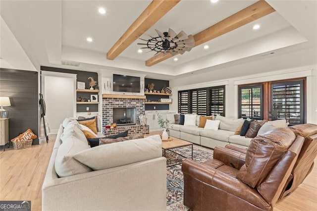 living room featuring ceiling fan, beamed ceiling, light hardwood / wood-style flooring, and a fireplace